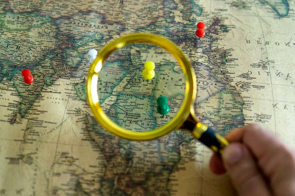 A magnifying glass over a detailed map with colorful location pins.