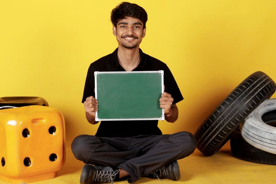 A cheerful person seated with a small green board in a bright everyday setting.