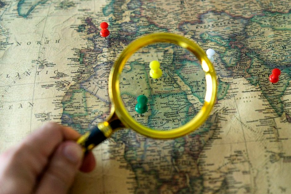 A magnifying glass held over a detailed map with colorful location pins.