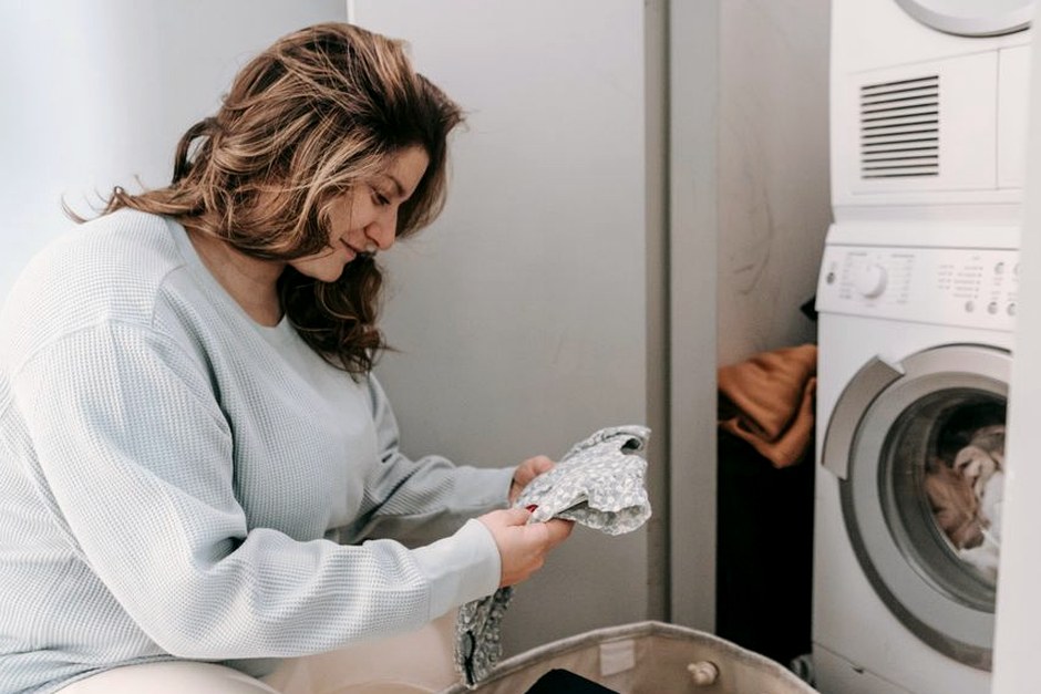 A person sorting everyday clothes beside a washing machine in a bright laundry area.