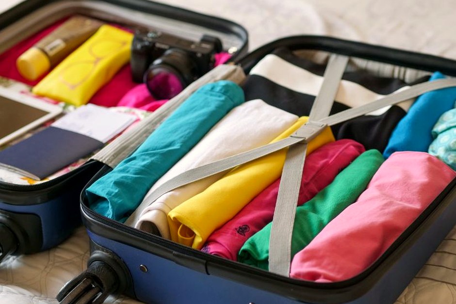 An open suitcase packed neatly with bright clothing and compact travel essentials.